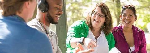 Four students sitting outside on campus, laughing